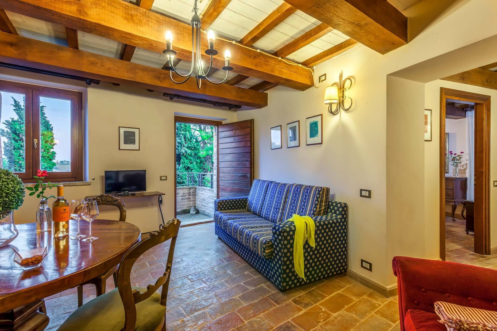 A cozy living room with a wooden ceiling, a patterned sofa, a dining table with chairs, and a television.