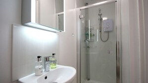 A bathroom with a white sink, two bottles of liquid soap, a glass shower enclosure, and a mirror above the sink. - Sea Tang Guest House (Brixham)