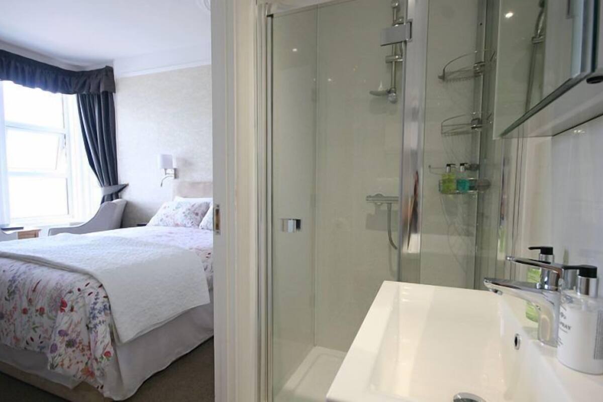 A hotel room with a bed, a shower area, and a bathroom with a sink and mirror.
