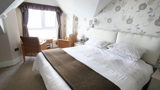 A neatly arranged hotel room with a large bed, a desk, and a chair. - Sea Tang Guest House (Brixham)