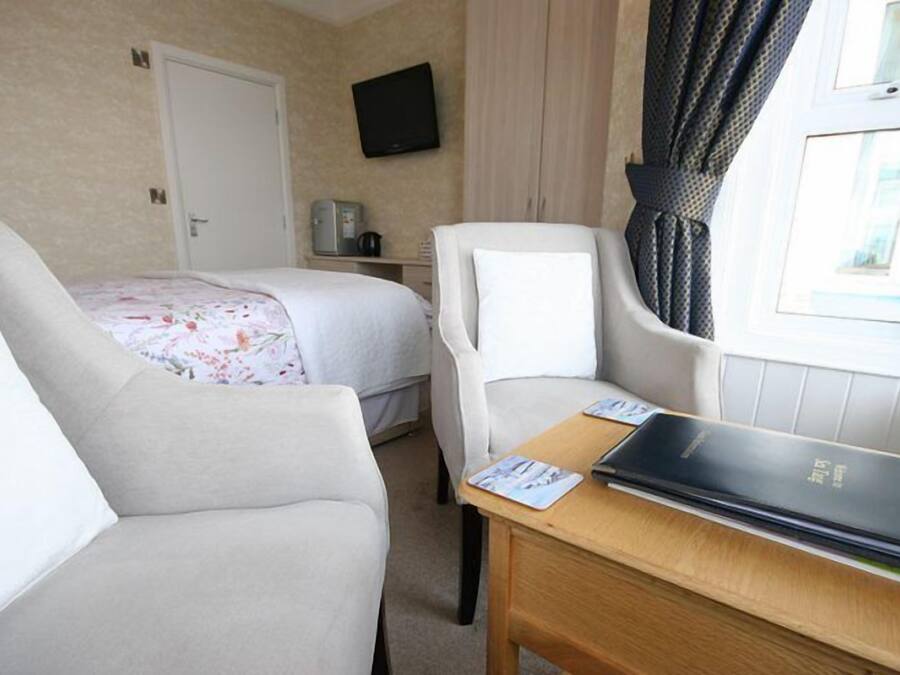 A hotel room with two beds, a desk, a chair, a TV, and a window with curtains.