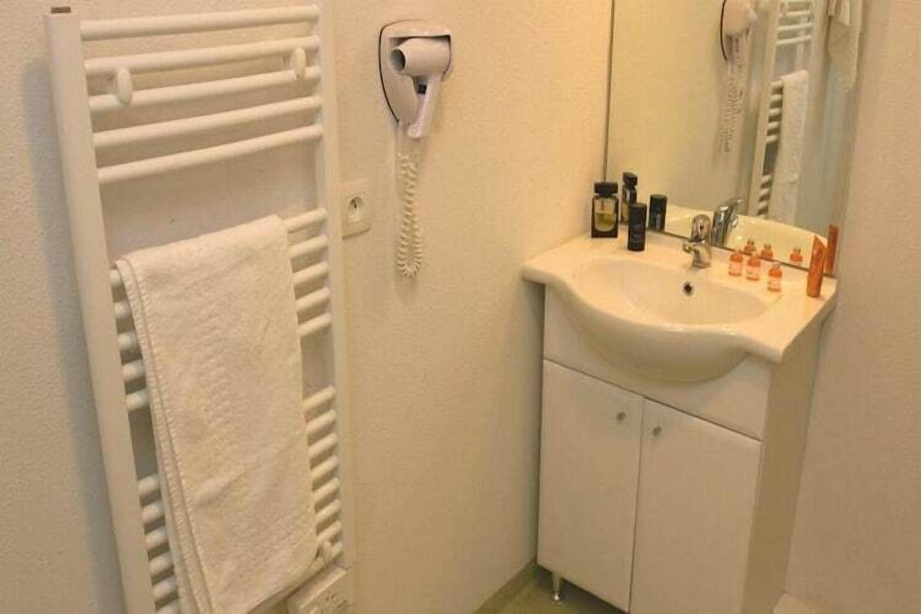 A bathroom with a white sink, mirror, towel rack, and a hairdryer.