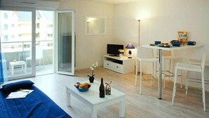 Ein modernes Wohnzimmer mit Sofa, Couchtisch, Fernseher und Essbereich mit Stühlen sowie einem Balkon.