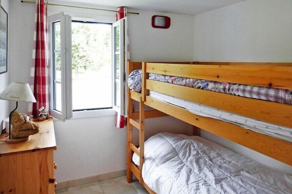 Ein Schlafraum mit Etagenbetten, einem Fenster, einem Schreibtisch mit Lampe und einem kleinen Schrank.