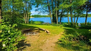 A campsite with a fire pit, surrounded by trees and a lake. - Great holiday home in the middle of nature and right on the lake, Natac Wielka (Natac Wielka)
