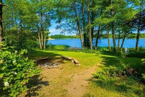 Un campamento con un brasero, rodeado de árboles y un lago.