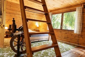 Interior de una cabaña de madera con una cama, una escalera, un ventanal y suelo de madera.