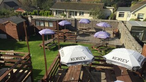 Outdoor seating with wooden tables and benches, surrounded by a stone wall. - Mounts Bay Inn (Helston)
