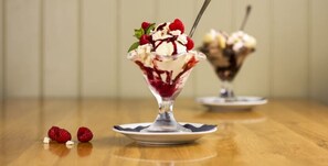 A dessert in a glass bowl with a spoon, placed on a wooden table. - Mounts Bay Inn (Helston)