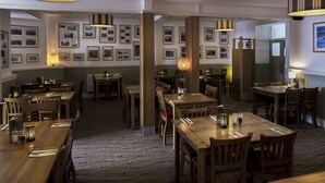 A spacious dining area with wooden tables and chairs, framed pictures on the walls, and pendant lighting. - Mounts Bay Inn (Helston)