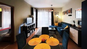 A modern living room with a sofa, a dining table with placemats, a TV, and a kitchen area with cabinets and a countertop. - Apartment in Swinoujscie near the Beach (Swinoujscie)
