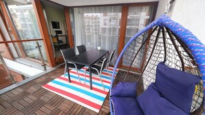 A balcony with a table and chairs, a striped rug, and a hanging chair with cushions. - Apartment in Swinoujscie near the Beach (Swinoujscie)