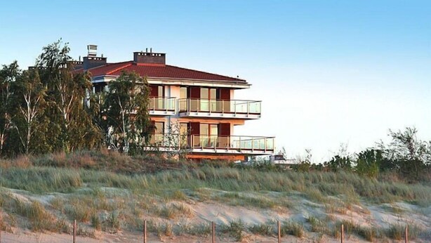 A two-story beachfront house with a red roof, multiple balconies, and a sandy beach in the foreground. - Apartment in Swinoujscie near the Beach (Swinoujscie)
