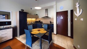 A compact kitchen with modern appliances, a dining area with blue chairs and yellow placemats, and a wooden cabinet. - Apartment in Swinoujscie near the Beach (Swinoujscie)