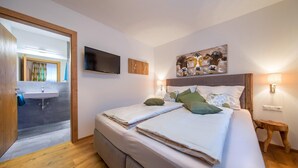 A bedroom with a bed, a TV, a painting, and a bedside lamp.