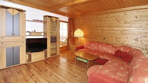 L’intérieur d’un chalet en bois, avec un canapé, un téléviseur, des placards et une lampe.