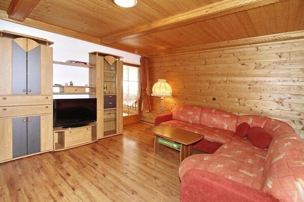 A wooden cabin interior with a sofa, TV, cabinets, and a lamp. - House in Krimml near Waterfalls & Hiking Trails (Krimml)