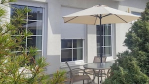 Une terrasse extérieure avec une table ronde et des chaises, un parasol beige et une plante en pot.