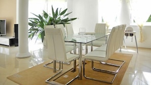 Un espace repas moderne avec une table en verre, des chaises blanches et une plante en pot.