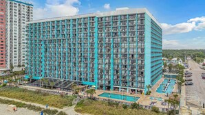 A high-rise hotel with a modern design, featuring a large pool area with multiple swimming options and a beach section. - Oceanfront King Suite with Sofa~Landmark 830 (Myrtle Beach)