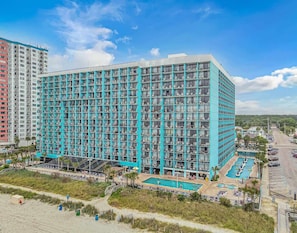 A high-rise hotel with a modern design, featuring a large pool area with multiple swimming options and a beach section.