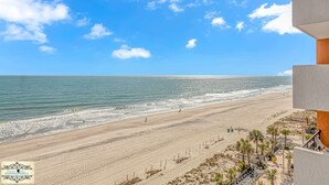A beach view from a balcony with a clear sky, sandy beach, and ocean. - Oceanfront King Suite with Sofa~Landmark 830 (Myrtle Beach)