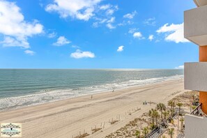 A beach view from a balcony with a clear sky, sandy beach, and ocean.