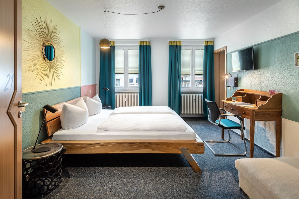 A hotel room with a bed, desk, chair, TV, and a window with curtains.