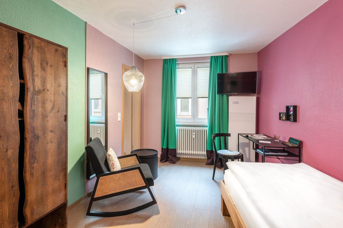 A room with a bed, a desk, a chair, a radiator, and a television.
