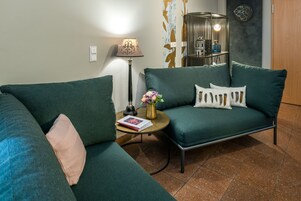 Una sala de estar moderna con un sofá verde, una mesita redonda con una lámpara y un jarrón decorativo.