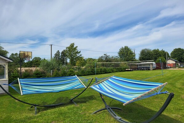 A grassy outdoor area with two hammocks and a basketball hoop.