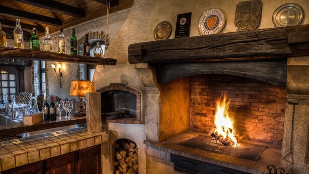 A rustic bar area with a brick fireplace, wooden shelves with bottles, and a tiled counter. - Landhaus Diedert (Wiesbaden)