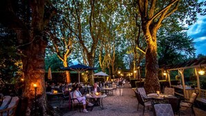An outdoor dining area with tables and chairs under trees, surrounded by a gravel path. - Landhaus Diedert (Wiesbaden)