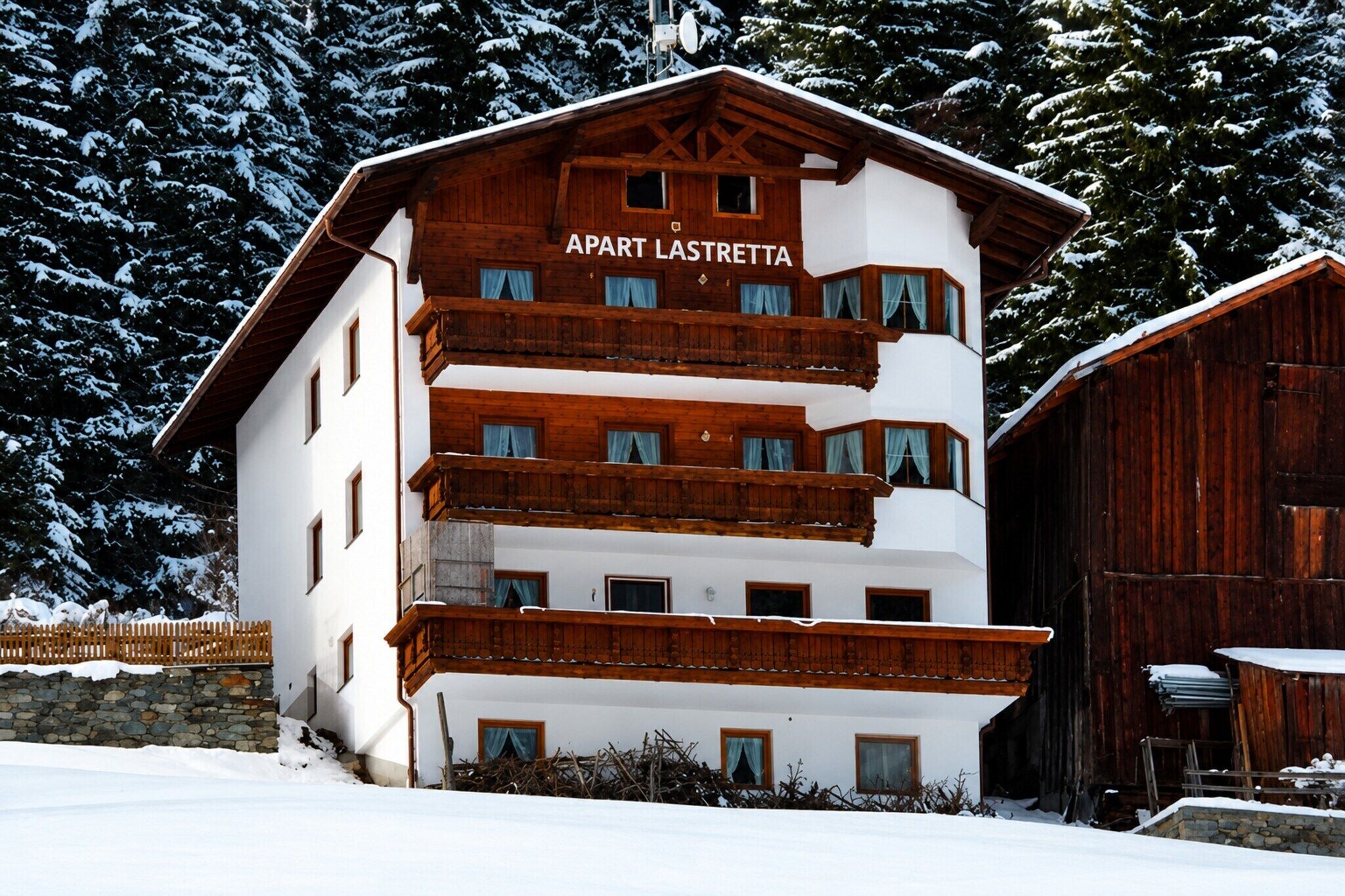 A multi-story building with 'APART LASTRETTA' signage, wooden balconies, and a stone wall foundation.