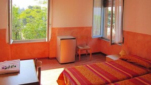 A room with two beds, a small table, a chair, a refrigerator, and a window with blinds. - Mobile home in Cisano San Vito caravan park (Cisano di Bardolino)