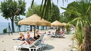A beach with thatched umbrellas and lounge chairs. - Mobile home in Cisano San Vito caravan park (Cisano di Bardolino)