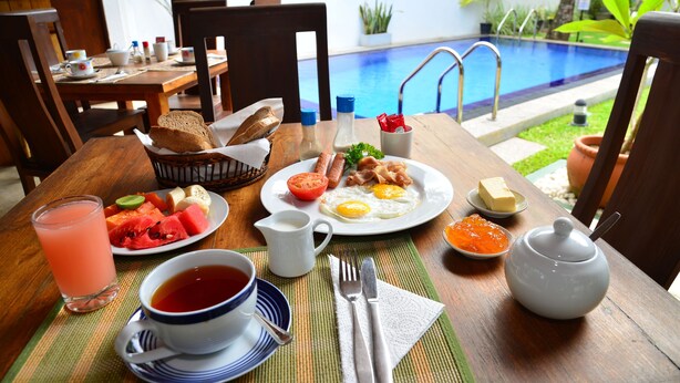Una mesa de desayuno con diversos alimentos, una taza de té y vista a una piscina.