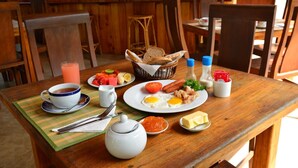 Una mesa de desayuno con platos de huevos, salchichas, tomates y pan, además de salsas y una taza de té.