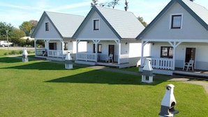 Eine Reihe weißer Cottagehäuser mit grauen Dächern, jedes mit einer Veranda und einer kleinen Terrasse.