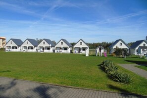 A row of white cottages with attached porches, a grassy lawn, and a playground with a slide.