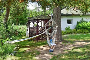 A hammock hanging between trees in a garden with a wooden gazebo in the background.