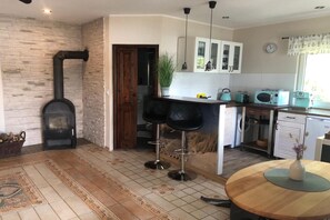 A kitchen with a stone wall, a wood-burning stove, bar stools, a sink, and a window with curtains.