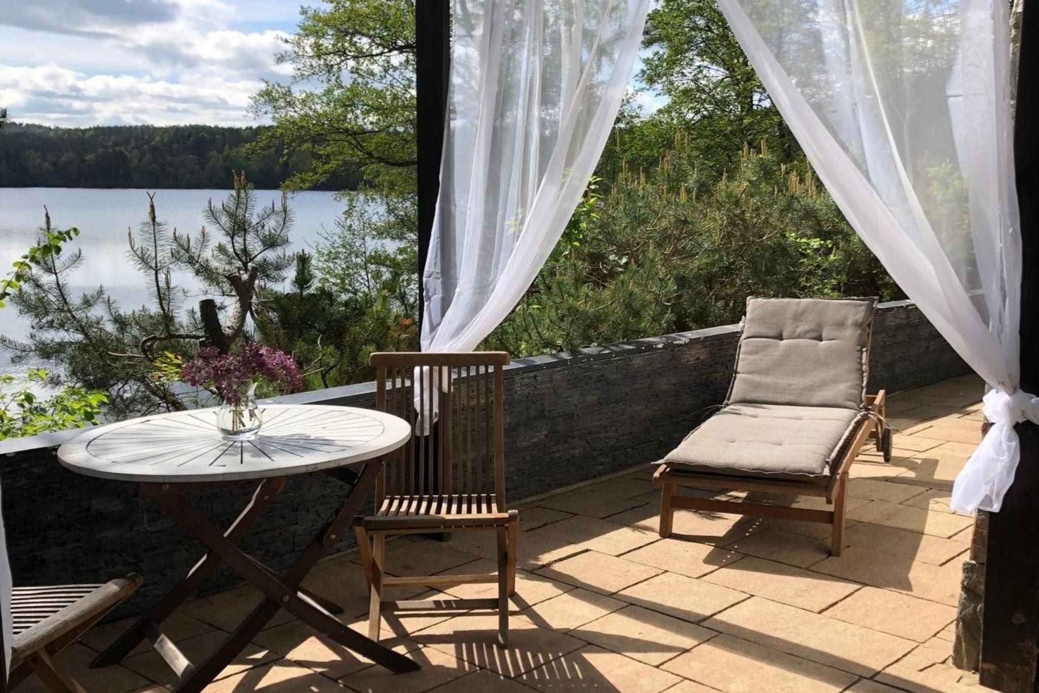 A patio with a round table, two chairs, and a view of a lake.