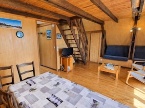 Une pièce chaleureuse avec un plafond en bois, un lit recouvert d’une courtepointe, un téléviseur posé sur un meuble en bois, un canapé et un escalier.