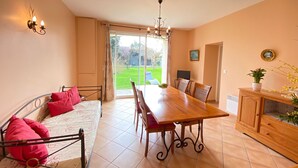 Une pièce comprenant un lit, une table à manger avec des chaises, un lustre et une vue sur un jardin, accessible par une porte coulissante.