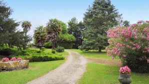 Un sentier de terre serpente à travers un jardin bien entretenu, où l’on trouve différentes espèces d’arbres et de plantes à fleurs.