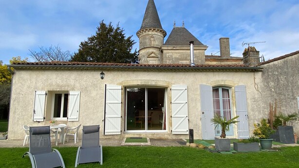 Une maison avec une tour, une terrasse avec des chaises et un petit jardin.