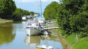 Un canal étroit où des bateaux sont amarrés le long des rives, le tout étant bordé d’une végétation luxuriante.