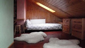 Un pequeño dormitorio con paneles de madera en el ático, techo inclinado, cama con ropa de cama estampada y una alfombra mullida blanca en el suelo.
