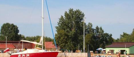 A red and white sailboat docked at a pier with a clear sky and trees in the background.